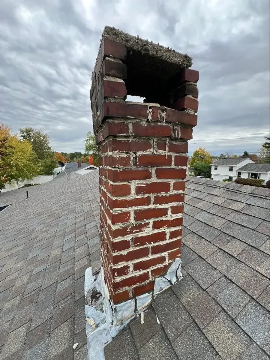 A brick chimney before repair — crumbling brickwork and an open, damaged stack